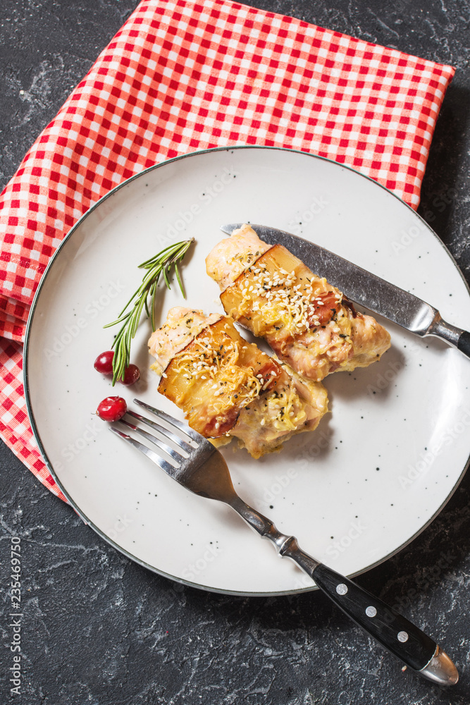 Stuffed chicken breast wrapped in bacon on a plate on stone table Stuffed chicken breast wrapped in bacon on a plate on stone table
