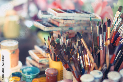 Paint brushes and watercolor paints on the table in a workshop, selective focus, close up.