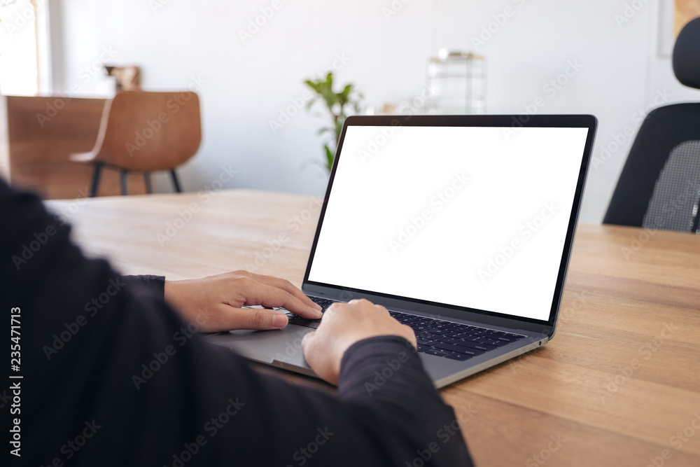 Mockup image of hands using and typing on laptop with blank white desktop screen on wooden table in office Mockup image of hands using and typing on laptop with blank white desktop screen on wooden table in office