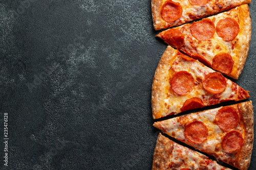 Cut into slices delicious fresh pizza with sausage pepperoni and cheese on a dark background. Top view with copy space for text. Pizza on the black concrete table. flat lay