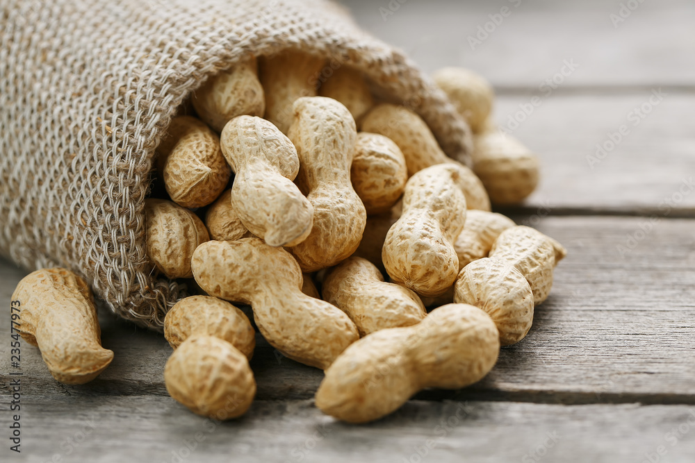 Peanuts in a miniature burlap bag on old, gray wooden surface Peanuts in a miniature burlap bag on old, gray wooden surface