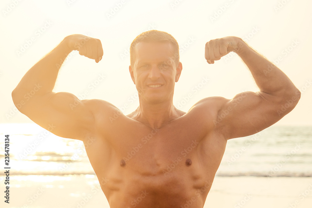 Handsome young muscular male model doing the workout stretching warm up on the beach summer.sexy athlete abs and perfect body in tropical paradise shore sunset Handsome young muscular male model doing the workout stretching warm up on the beach summer.sexy athlete abs and perfect body in tropical paradise shore sunset