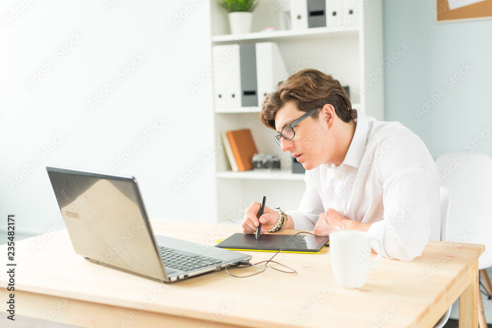 Business, design and people concept - Handsome young man in white shirt using graphic tablet at wooden table Business, design and people concept - Handsome young man in white shirt using graphic tablet at wooden table