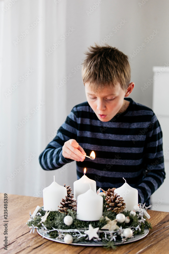Young boy lighting the first candle on Advent Wreath on the first Sunday in December. Celebrating Christmas holidays, swiss tradition. Young boy lighting the first candle on Advent Wreath on the first Sunday in December. Celebrating Christmas holidays, swiss tradition.