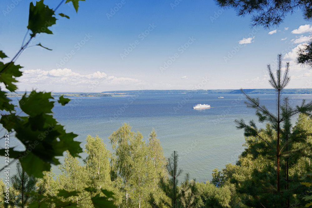 view through the green forest to the river with a passenger ship view through the green forest to the river with a passenger ship