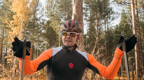 Training an athlete on the roller skaters. Biathlon ride on the roller skis with ski poles, in the helmet. Autumn workout. Roller sport. Adult man riding on skates. Athlete is getting ready to start. photo