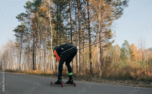 Training an athlete on the roller skaters. Biathlon ride on the roller skis with ski poles, in the helmet. Autumn workout. Roller sport. Adult man riding on skates. photo