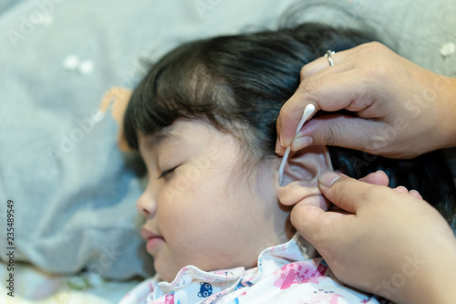 cleaning ear by cotton swab. Mother using cotton swab to clean the ear wax from her little baby's ear. Selective focus