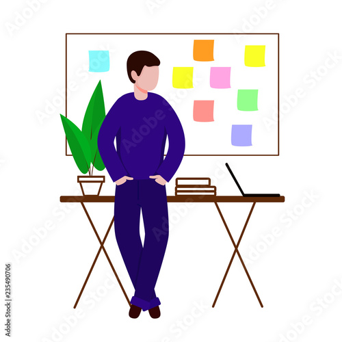 The guy in the workplace stands with his hands in his pockets. Behind him is a Board with stickers on it.