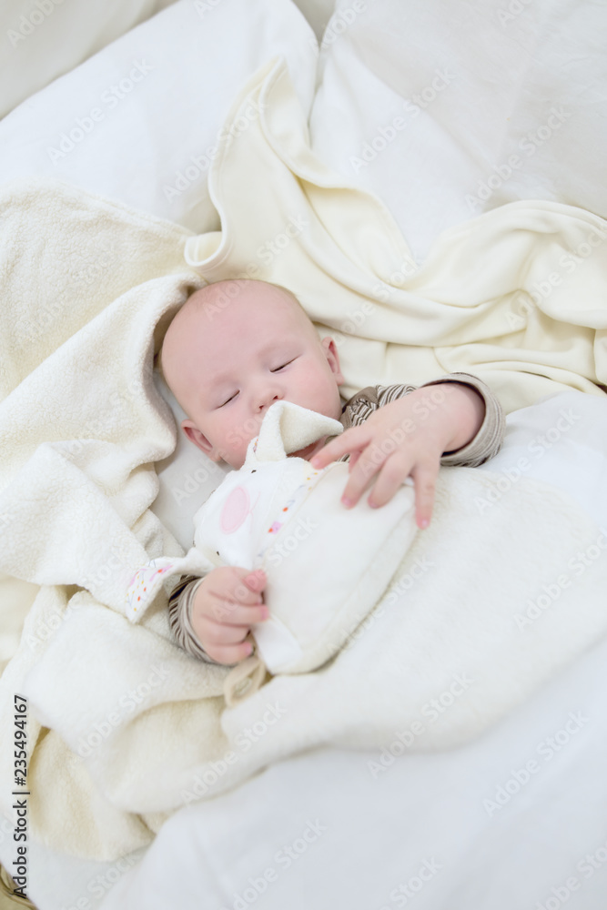 Baby boy in white sunny bedroom. Newborn child sleeping in white bed. Nursery for children. Textile and bedding from bio cotton for kids. New born kid with bio cotton blanket. Baby boy in white sunny bedroom. Newborn child sleeping in white bed. Nursery for children. Textile and bedding from bio cotton for kids. New born kid with bio cotton blanket.