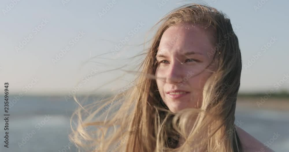 Slow motion closeup portrait of young girl standing on a beach and wind blows her hair