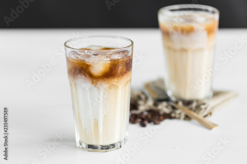 Ice coffee in a glass with cream over and coffee beans on the table