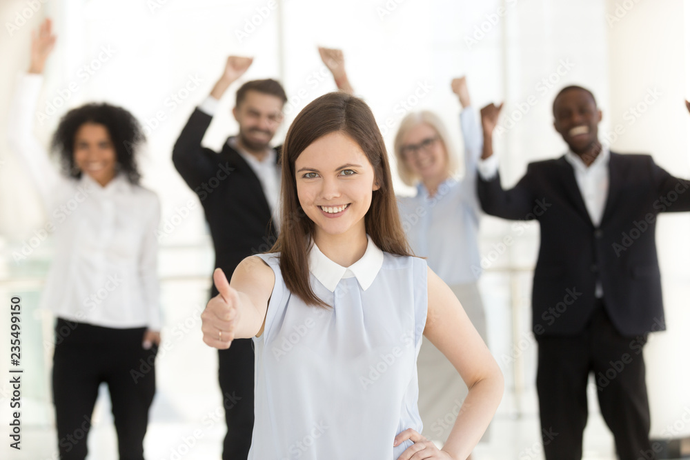 Happy client showing thumbs up satisfied with good service, excited business team people at background, young smiling woman raising finger as concept of best choice approval, recommendation, portrait Happy client showing thumbs up satisfied with good service, excited business team people at background, young smiling woman raising finger as concept of best choice approval, recommendation, portrait