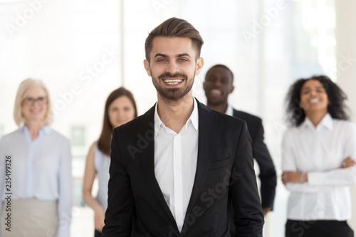 Smiling excited young businessman in suit looking at camera posing with diverse team, millennial professional manager, corporate leader, successful executive, happy ceo or business coach portrait