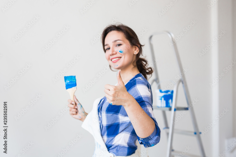 Repair, renovation and people concept - young woman painting the wall and looks like very happy, she showing thumb up Repair, renovation and people concept - young woman painting the wall and looks like very happy, she showing thumb up