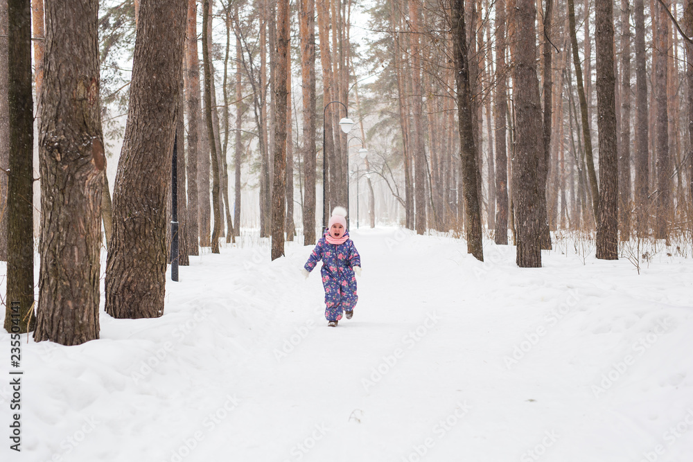 Childhood, nature and winter concept - Funny laughing toddler girl running in a beautiful snowy park
