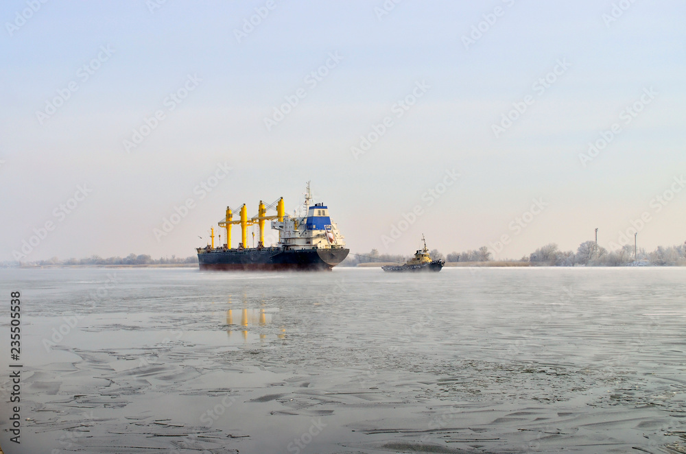 Tugboat pulls a freighter on a frozen river on a sunny day in winter. Tugboat pulls a freighter on a frozen river on a sunny day in winter.