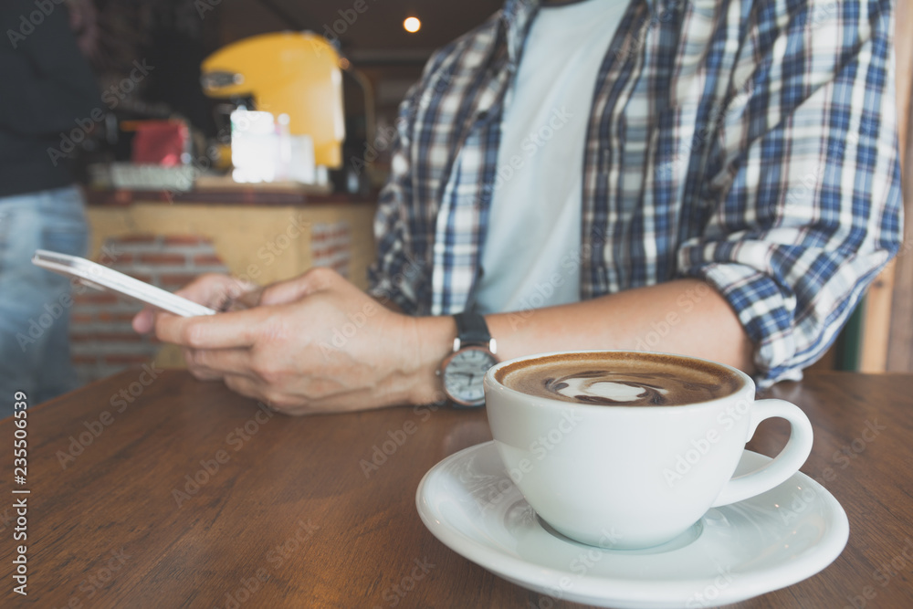 Male using a smart phone with coffee cup on wooden table. Male using a smart phone with coffee cup on wooden table.