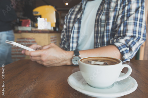 Male using a smart phone with coffee cup on wooden table.
