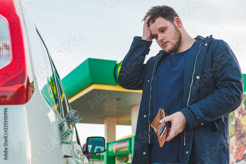 man with sad view and empty wallet at gas station. dollars money in car tank
