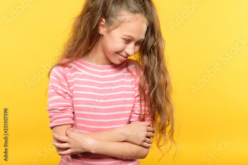 cute smiling shy girl. embarrassed child portrait on yellow background. emotion and facial expression concept.