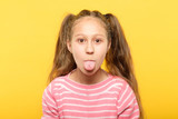girl on yellow background sticking tongue out. cute antics and frolicking concept.