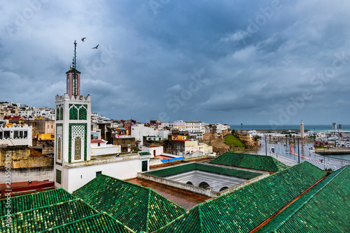 TANGIER / MOROCCO - NOVEMBER 2018: tiled roofs of buildings one of the many mosques of the medina of Tangier with a minaret and the kasbah / medina old quarter behind during the rain. 