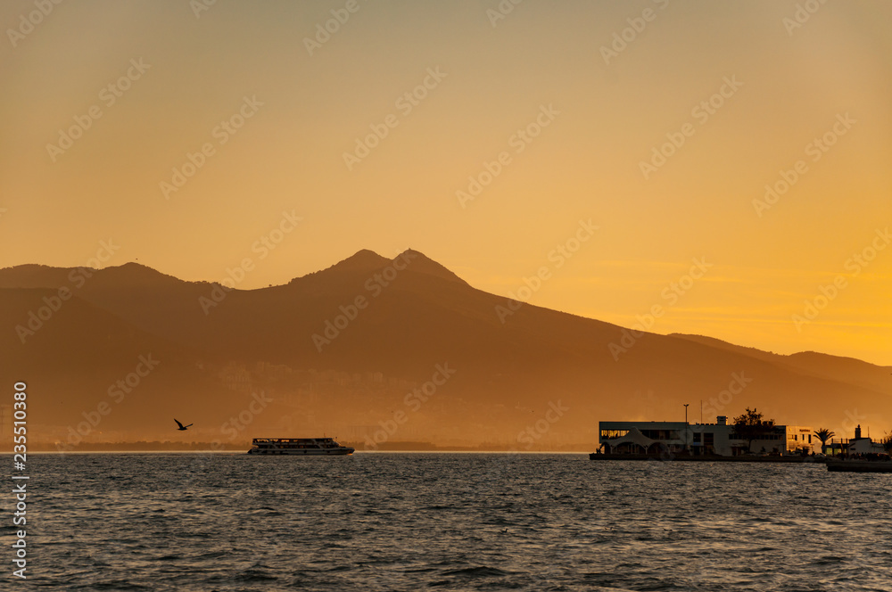 Landscape of Izmir city, foggy mountains, seagull and passenger ship at sunset.