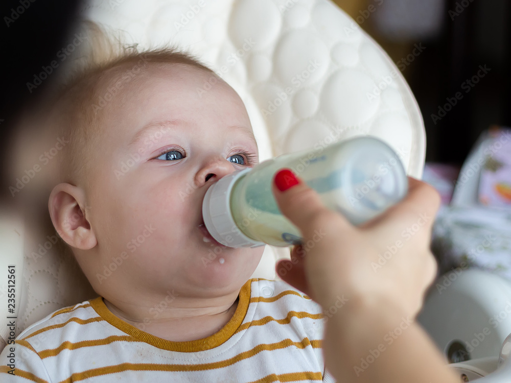 baby drinking milk from baby bottle while looking his mom. Mother feeding son infant from bottle. feeding from the bottle at home. baby drinking milk from baby bottle while looking his mom. Mother feeding son infant from bottle. feeding from the bottle at home.