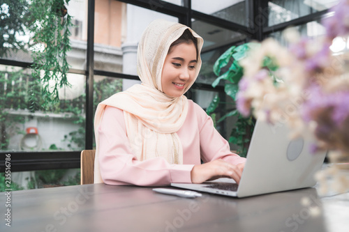 Beautiful young smiling asian muslim woman working on laptop sitting in living room at home. Asian business woman working document finance and calculator in her home office. Enjoying time at home.