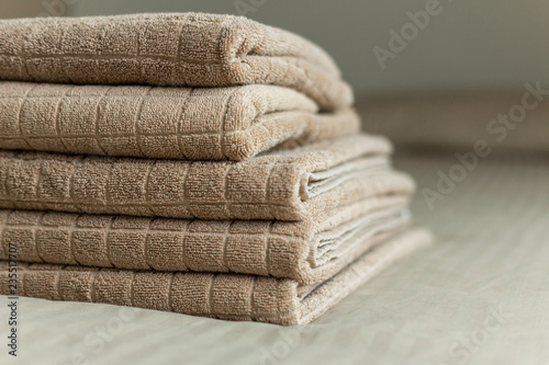 Stack of beige hotel towel on bed in bedroom interior.