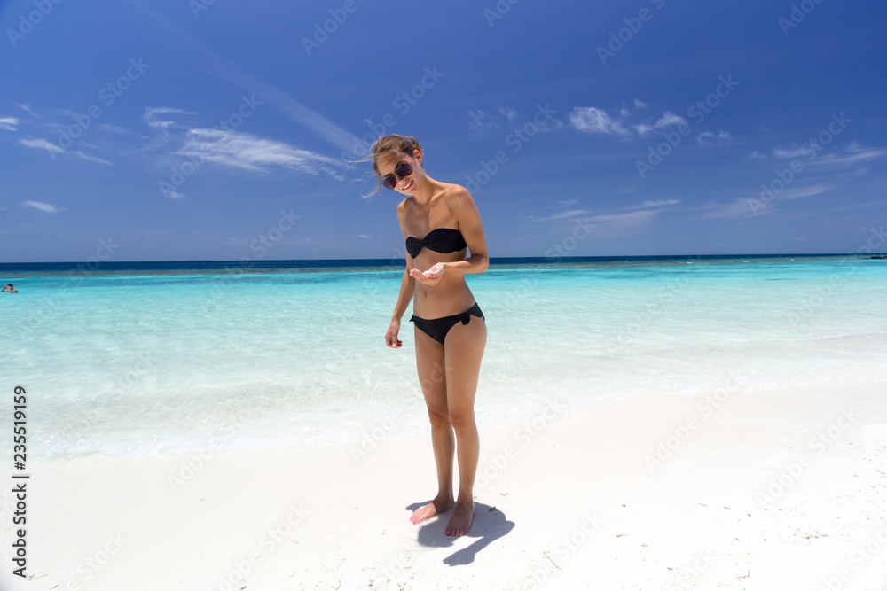 Junge Frau lacht an einem traumhaften Strand und zeigt eine Muschel