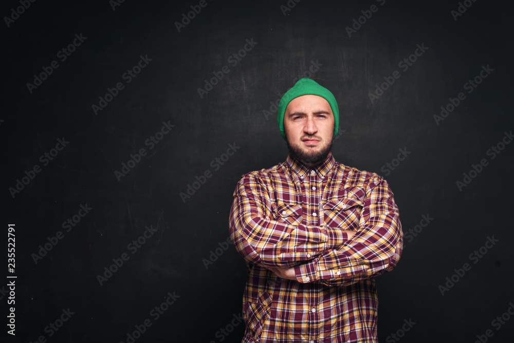 Young european man with beard in green knitted hat, looks serious and puzzled. Black background, blank copy space for text or advertisement