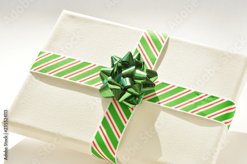 Obraz na plátně Close up of white canvas wrapped as a Christmas gift or present with striped ribbon in red, white and green, and green bow, on white background