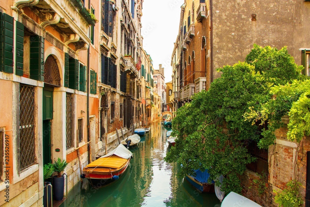 Small colourful scenic canal with ancient buildings and boats in Venice, Italy.