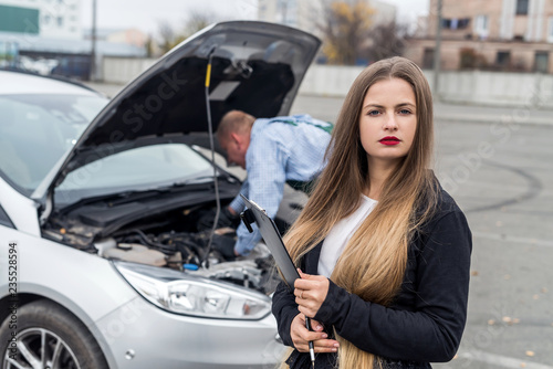 Young woman with clipboard and worker repairing car