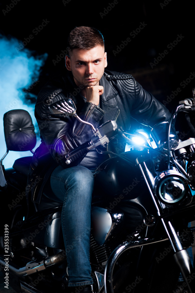 Fototapeta Cute biker in leather jacket sits on a motorcycle in blue smoke