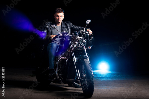 Cute biker in leather jacket sits on a motorcycle in blue smoke  © Rakursstudio