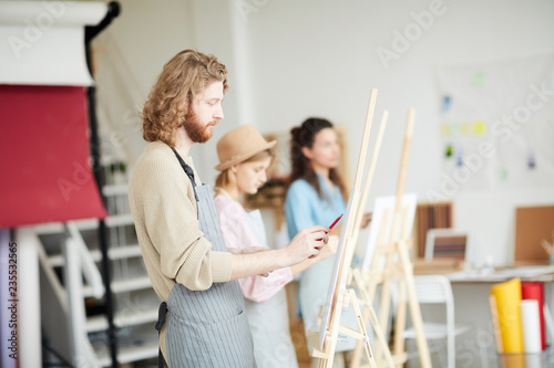Contemporary young artist standing in front of easel in studio while sketching on paper