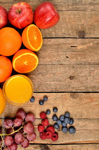 Orange juice, fresh oranges, apples, grapes, raspberries and blueberries on a wooden table - view from above - vertical photo - left orientation frame photo