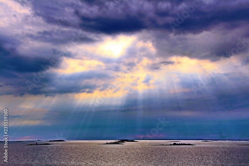 The sun behind the clouds with rays of light shining down on sea