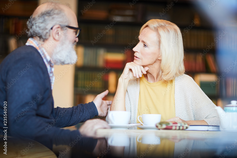 Blonde aged woman looking at bearded man during their conversation by cup of tea in cafe