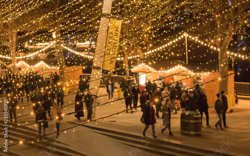 Valokuvatapetti Blurred background of bright festive lights on a busy evening street