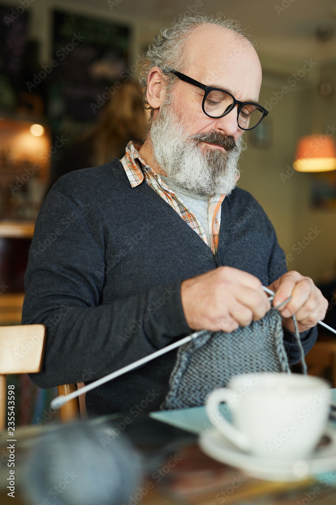 Φωτογραφία Bearded mature man concentrating on knitting warm winterwear by cup of tea