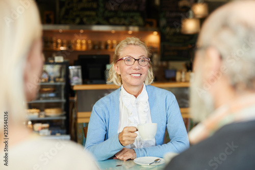 Happy blonde with toothy smile having tea with her friends during conversation in cafe