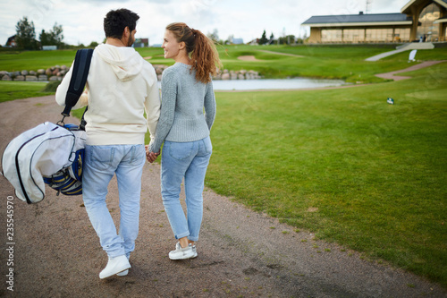 Young casual couple holding by hand while discussing their golf play on way home