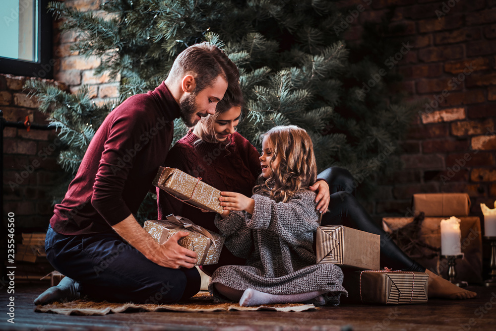 Attractive family opens presents while sitting on a floor next to the Christmas tree. 