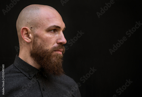 bald man with a beard in a black shirt on a dark background