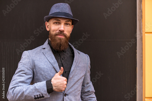 stylish man with a beard in a hat on the street showing hand signs