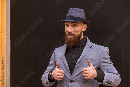stylish man with a beard in a hat on the street showing hand signs